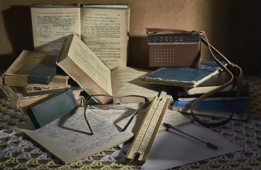Still life of a classic study setting with vintage books, glasses, slide rule, and an old analog radio.